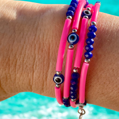 Close-up of a wrist wearing pink and blue beaded bracelets with a blurred blue background