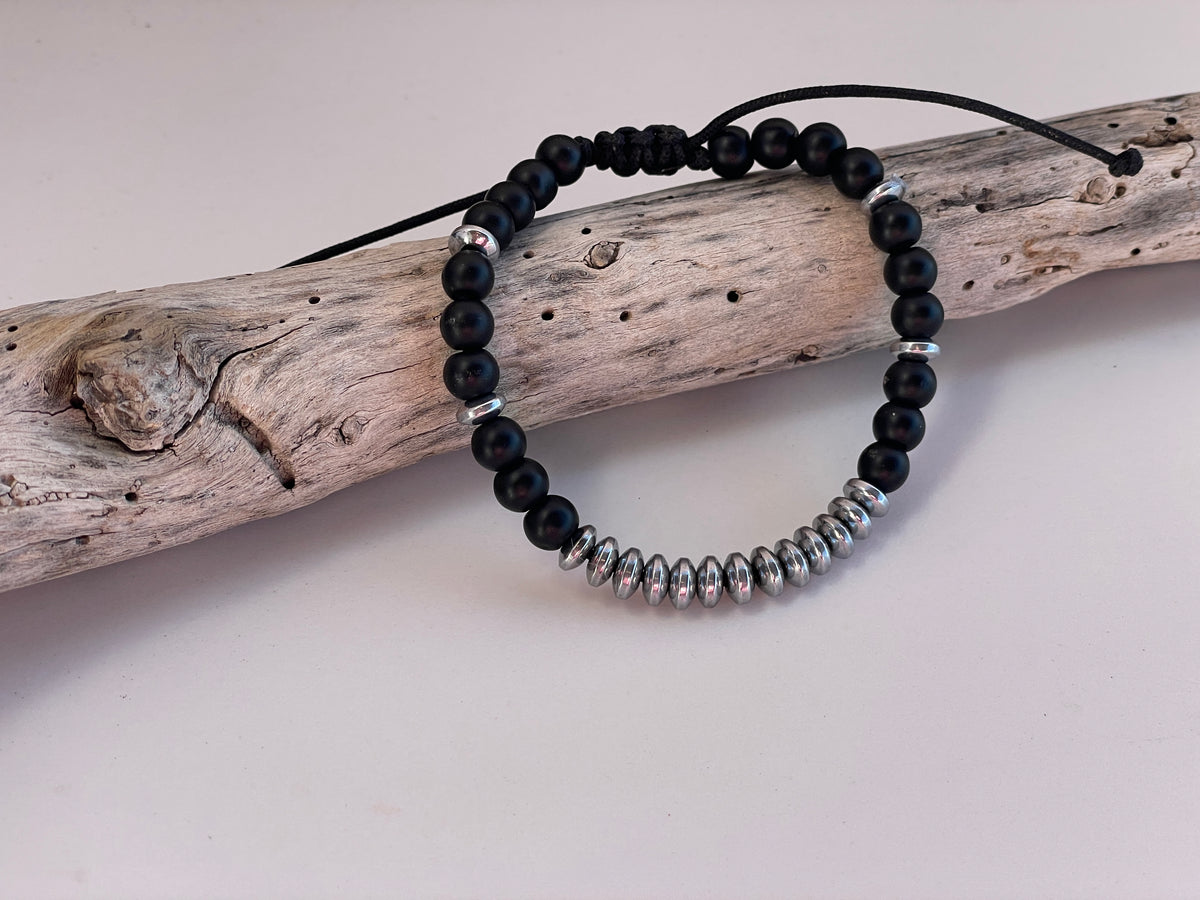 Black beaded bracelet with silver accents on a piece of driftwood.