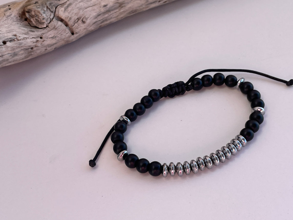 Black beaded bracelet with silver accents on a light pink background
