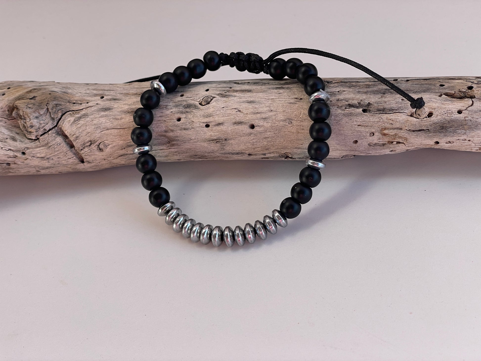 Black beaded bracelet with silver accents on a piece of driftwood against a light background