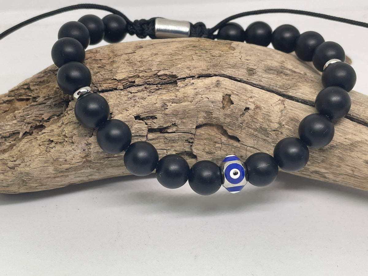 Black beaded bracelet with a blue and white evil eye charm on a wooden surface