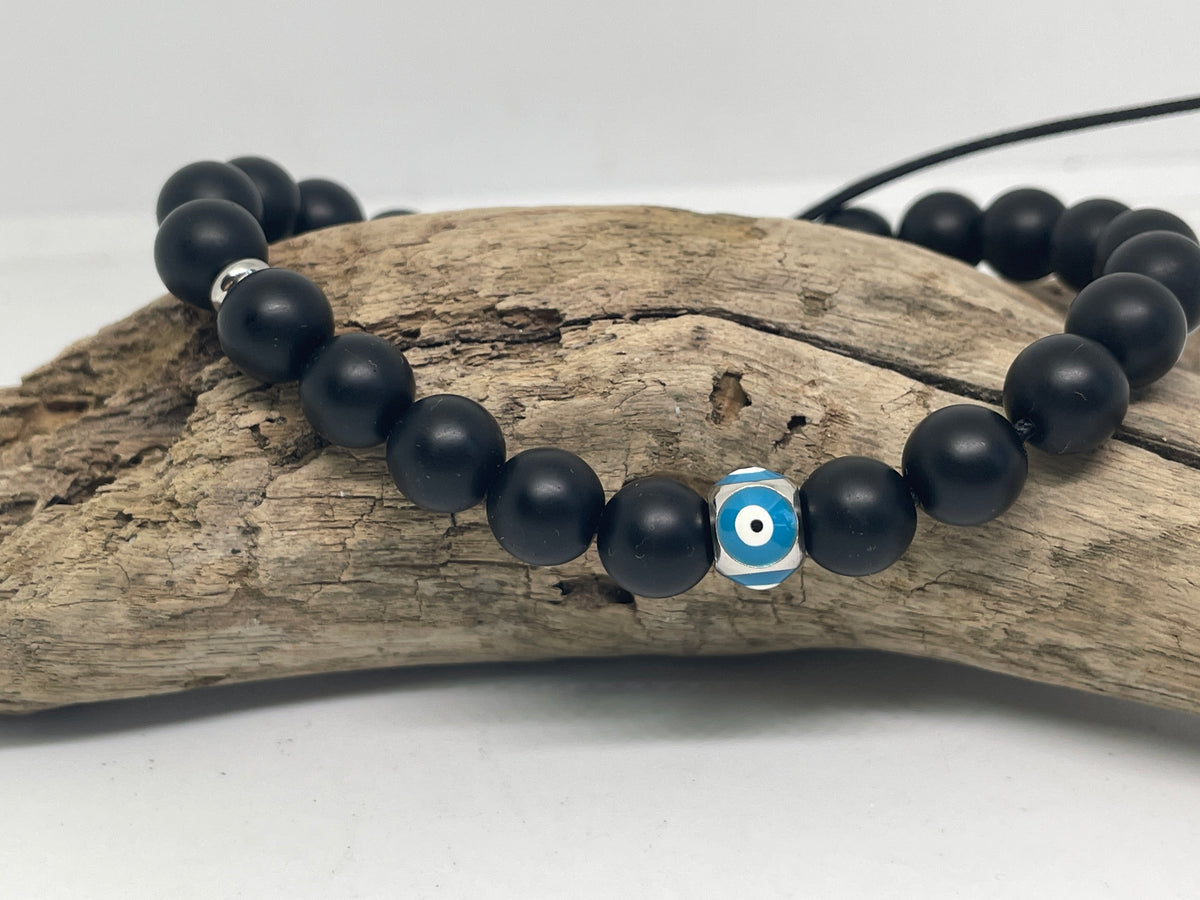 Black beaded bracelet with a blue and white evil eye charm on a piece of driftwood.