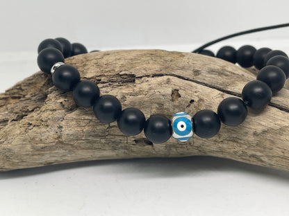 Black beaded bracelet with a blue and white evil eye charm on a piece of driftwood.