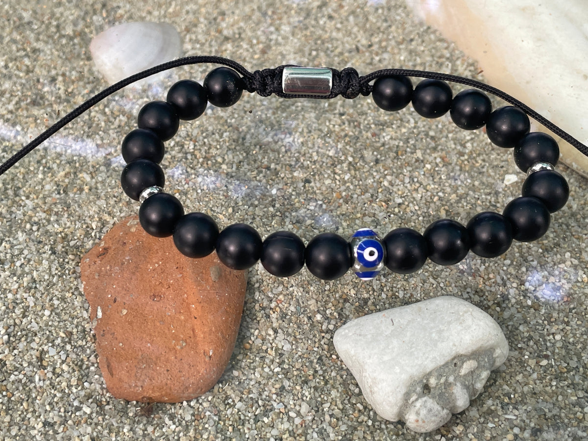 Black beaded bracelet with a blue evil eye charm on a sandy surface