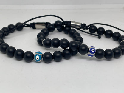 Black beaded bracelets with blue evil eye charms on a white background