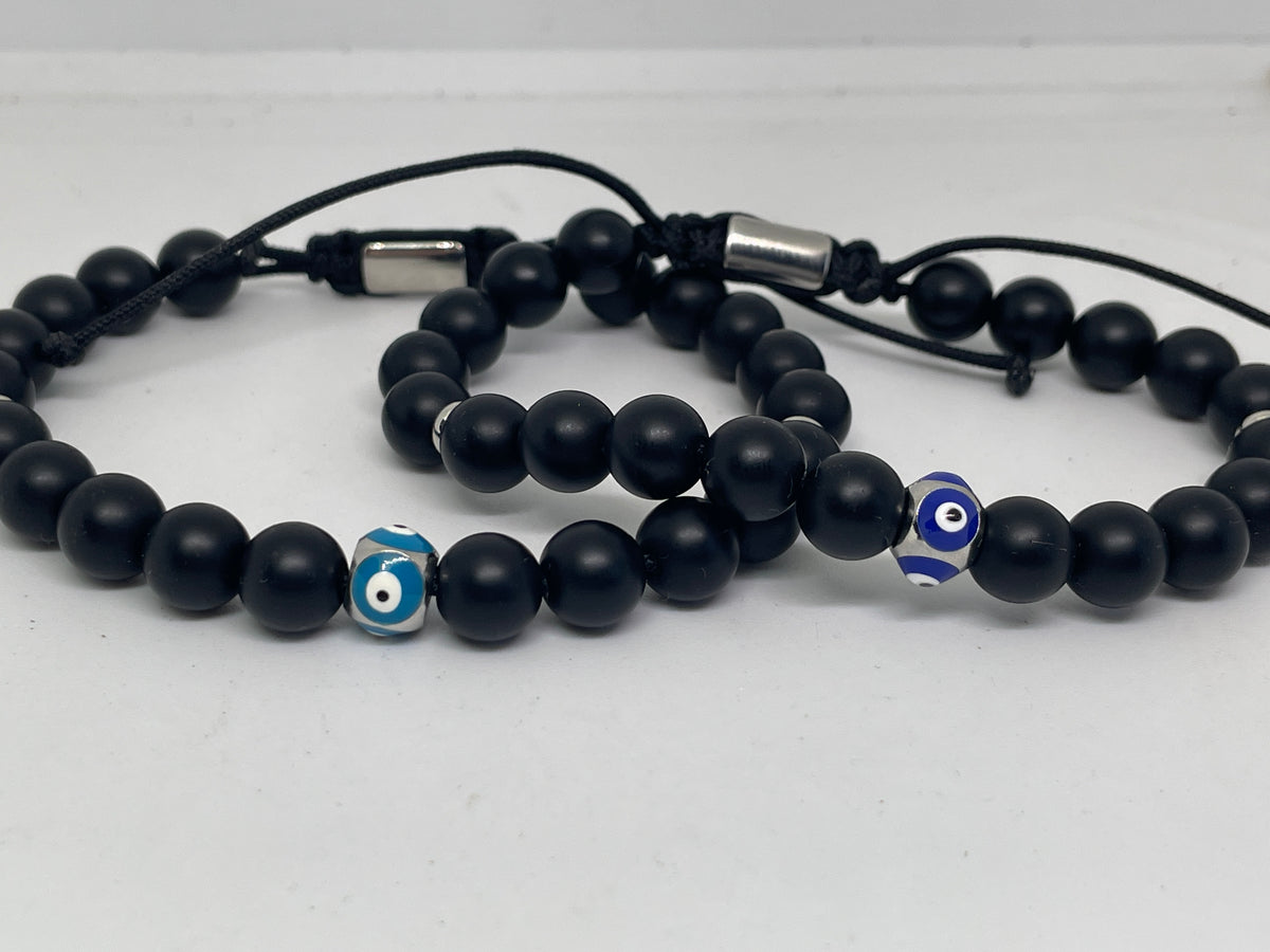 Black beaded bracelets with blue evil eye charms on a white background