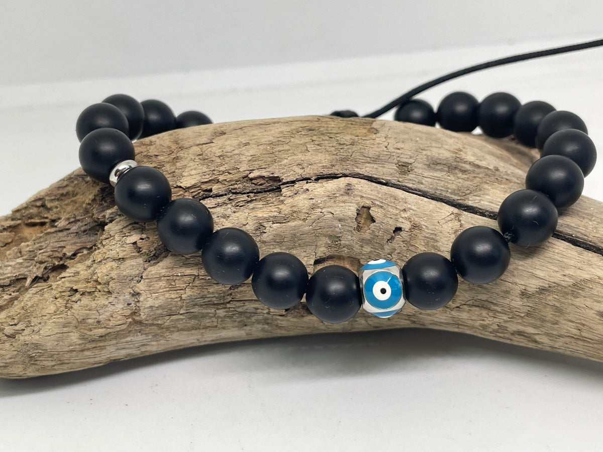 Black beaded bracelet with a blue evil eye charm on a piece of driftwood.