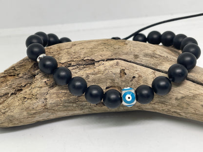 Black beaded bracelet with a blue evil eye charm on a piece of driftwood.