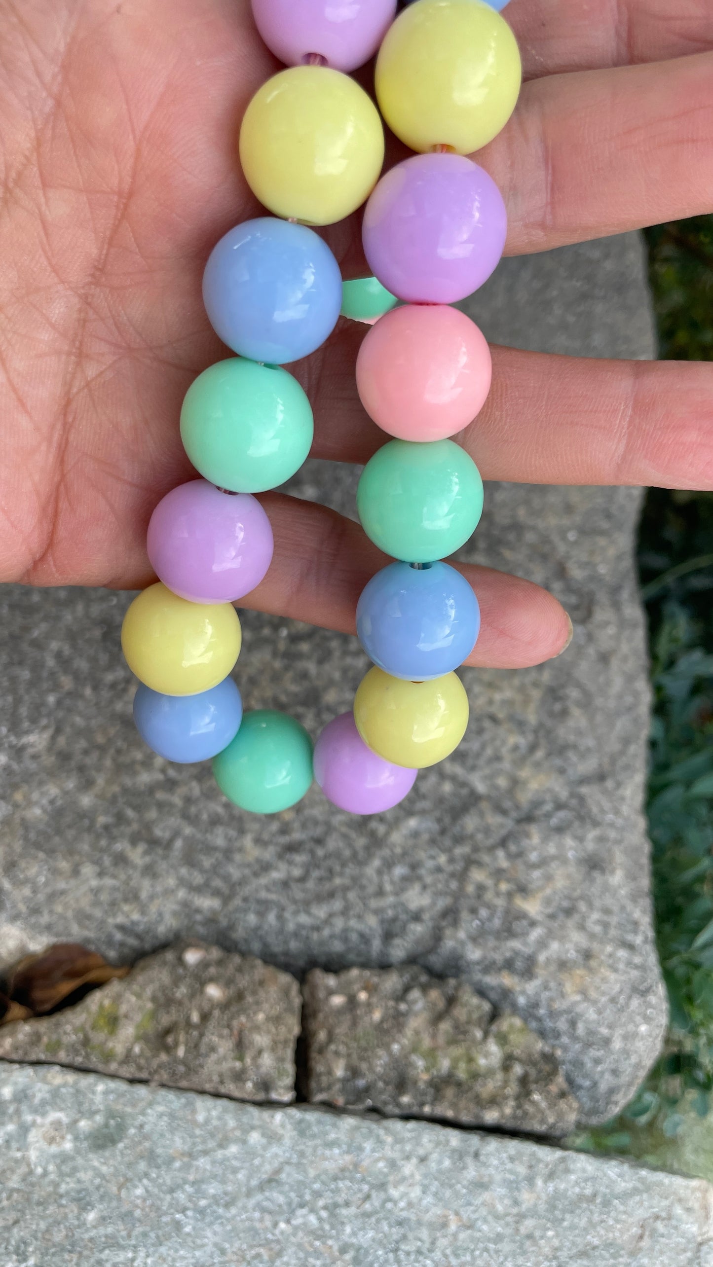 Pastel-colored beaded bracelet held by a hand on a stone surface