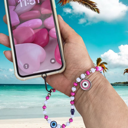 Hand holding a phone with a colorful beaded strap against a beach background