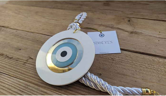 Evil eye pendant with white cord on a wooden surface, featuring the brand 'EyesOn'.