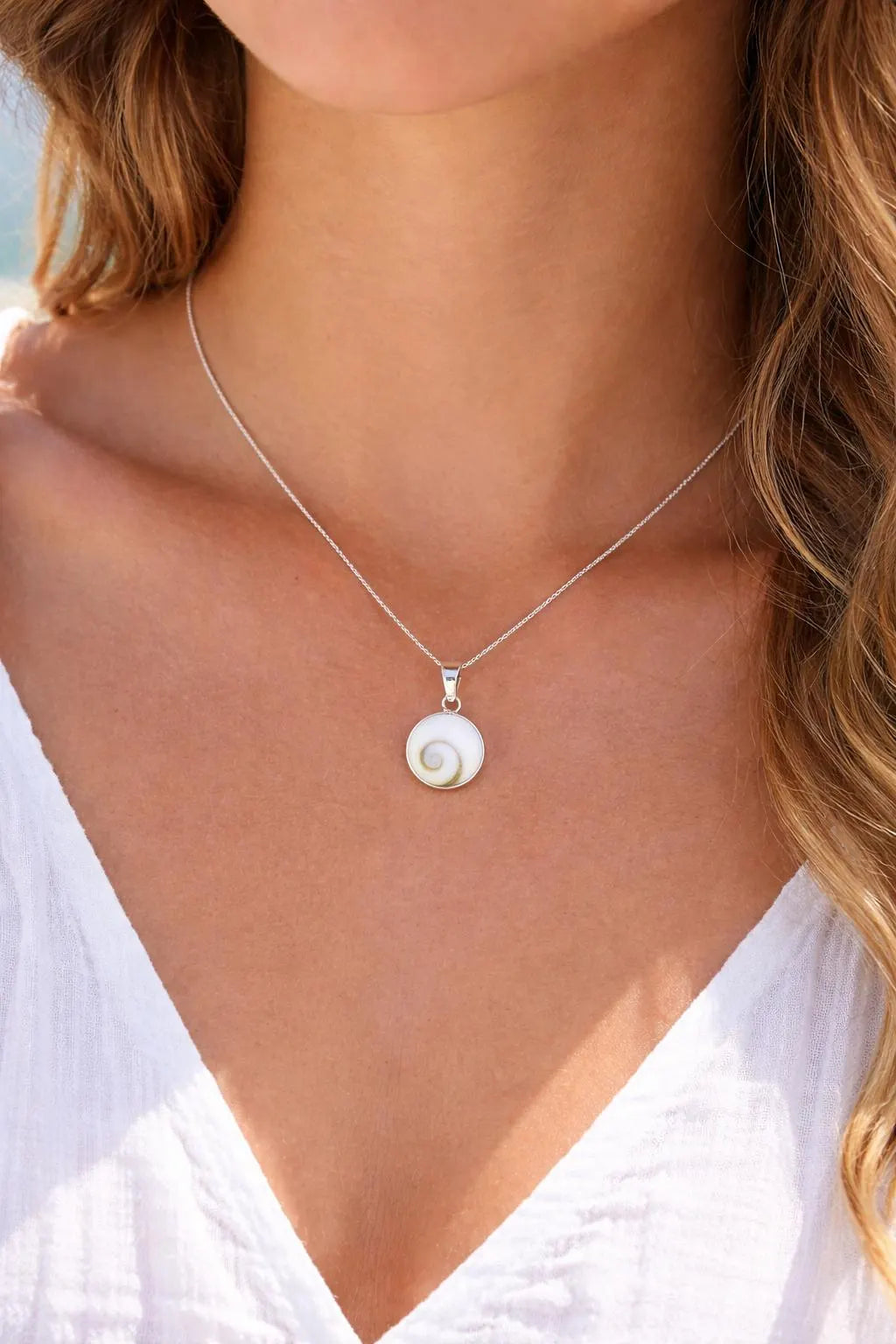 Necklace with a shell pendant worn by a person in a white top.