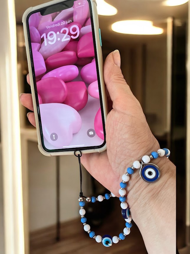 Hand holding a smartphone with a colorful screen, wearing a bracelet with blue and white beads.