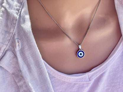 A close-up image of a person wearing a stainless steel necklace with a round blue glass evil eye charm pendant.
