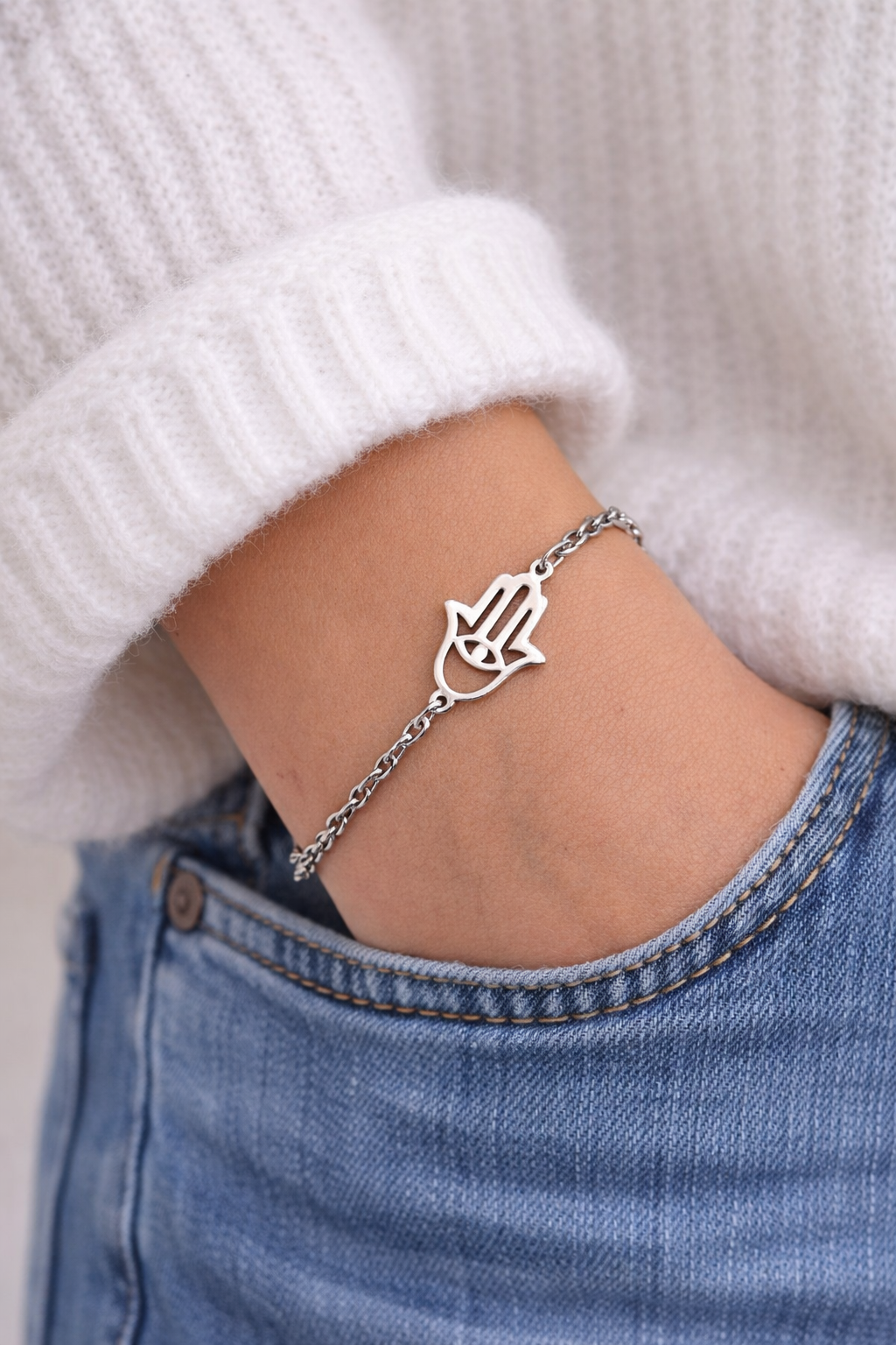 Silver Hamsa hand bracelet on a wrist with a white sweater and blue jeans.