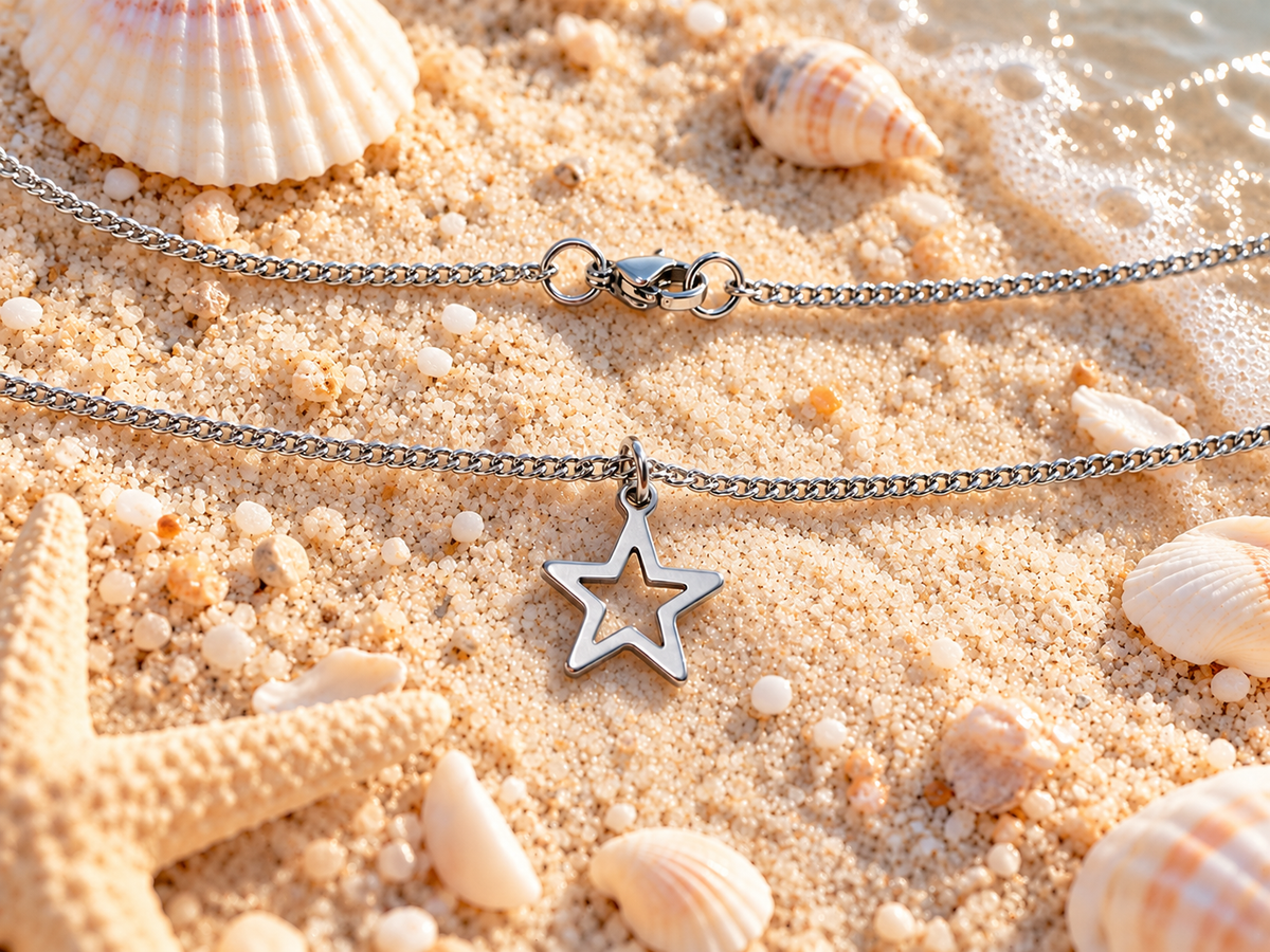 Two silver chain necklaces with star-shaped pendants, displayed on a sandy beach with seashells and a starfish.