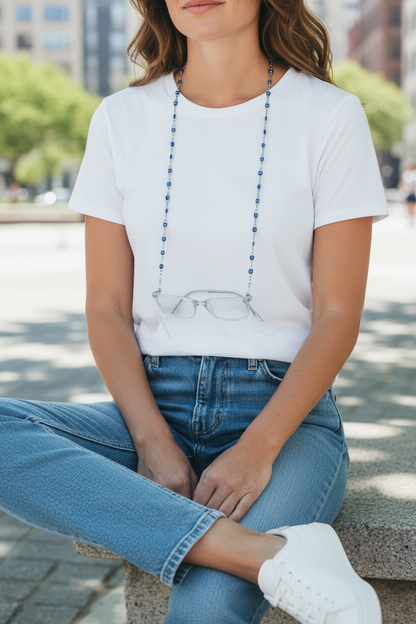 Person wearing a white t-shirt with a graphic of glasses and blue jeans, sitting outdoors.