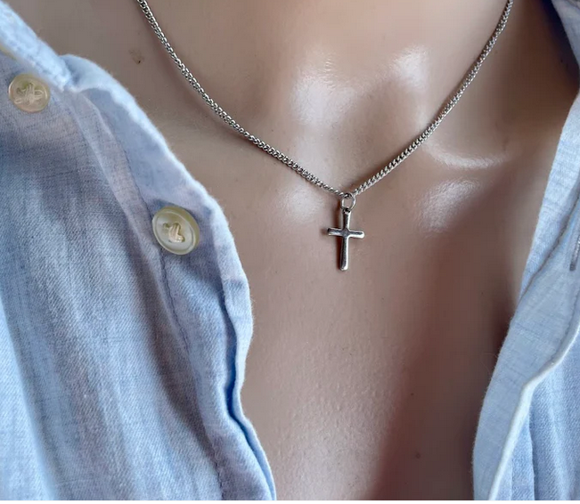 Silver cross necklace on a mannequin with a light blue shirt.