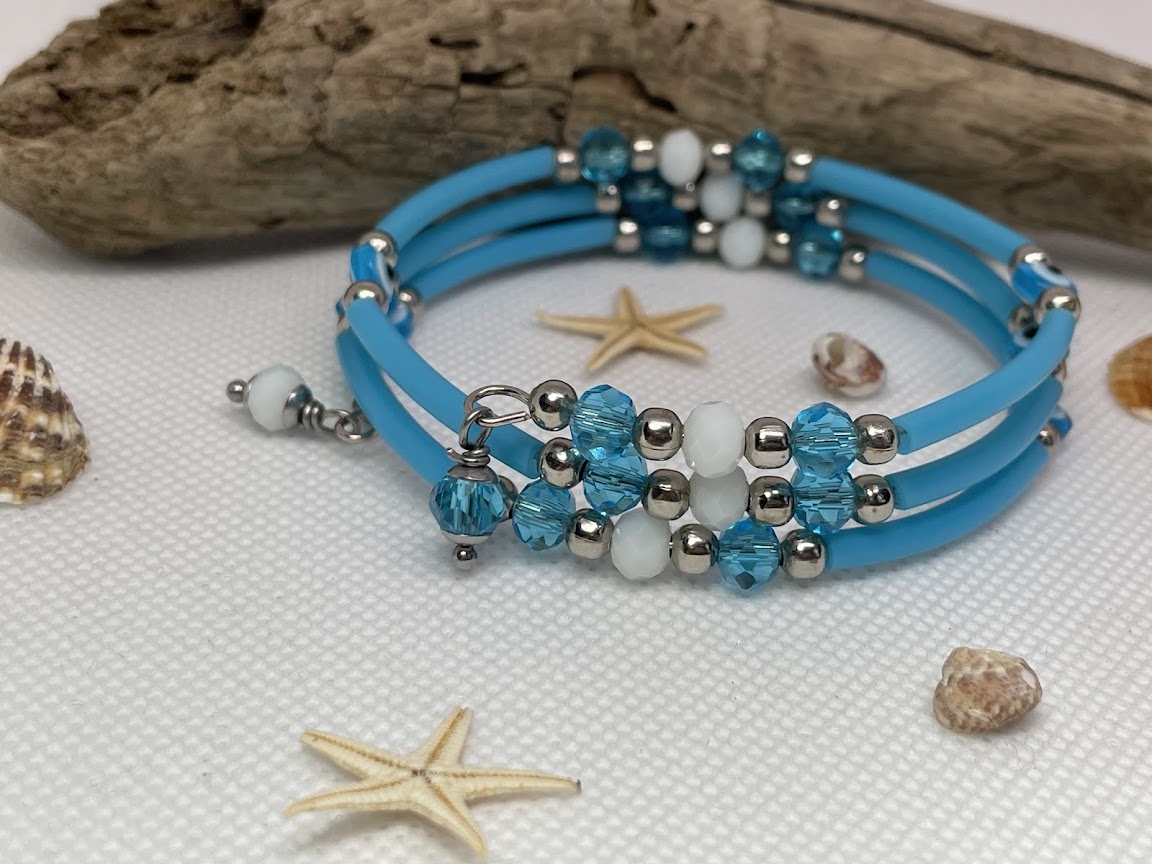 Blue beaded bracelet with silver accents on a textured surface with starfish and shells.