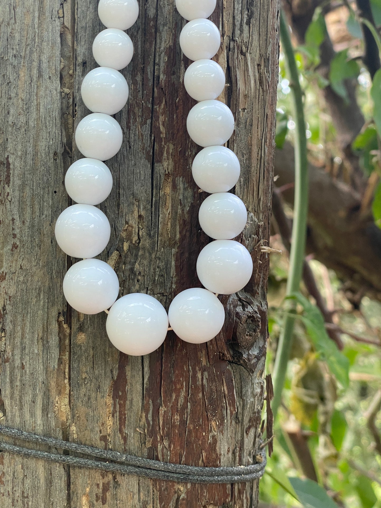 White beads on a string lying on a wooden surface with a natural background