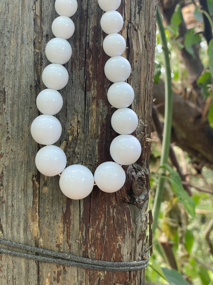 White beads on a string lying on a wooden surface with a natural background