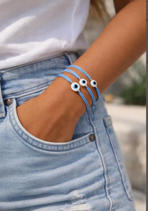 Close-up of a wrist wearing a blue bracelet with eye charms, against a blurred background.