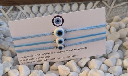Three blue hair ties with eye designs on a card, placed on pebbles.