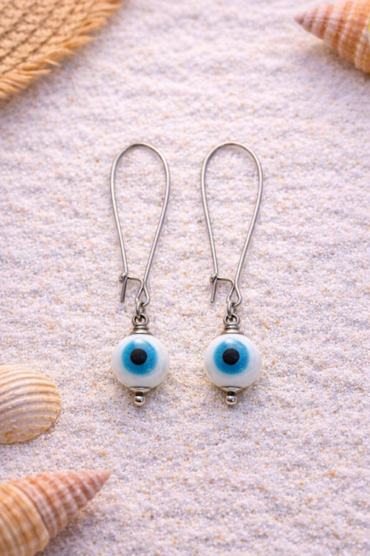 Pair of silver earrings with blue and white circular stones on a sandy background with shells.