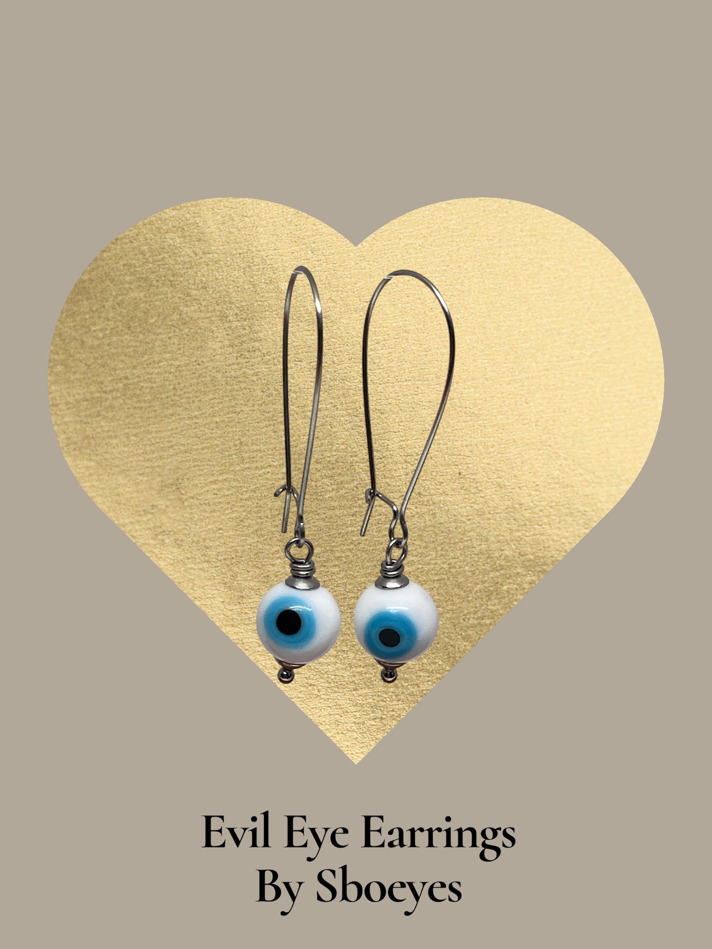Evil eye earrings with blue and black eyes on a gold heart-shaped background, branded 'Sboeyes'.