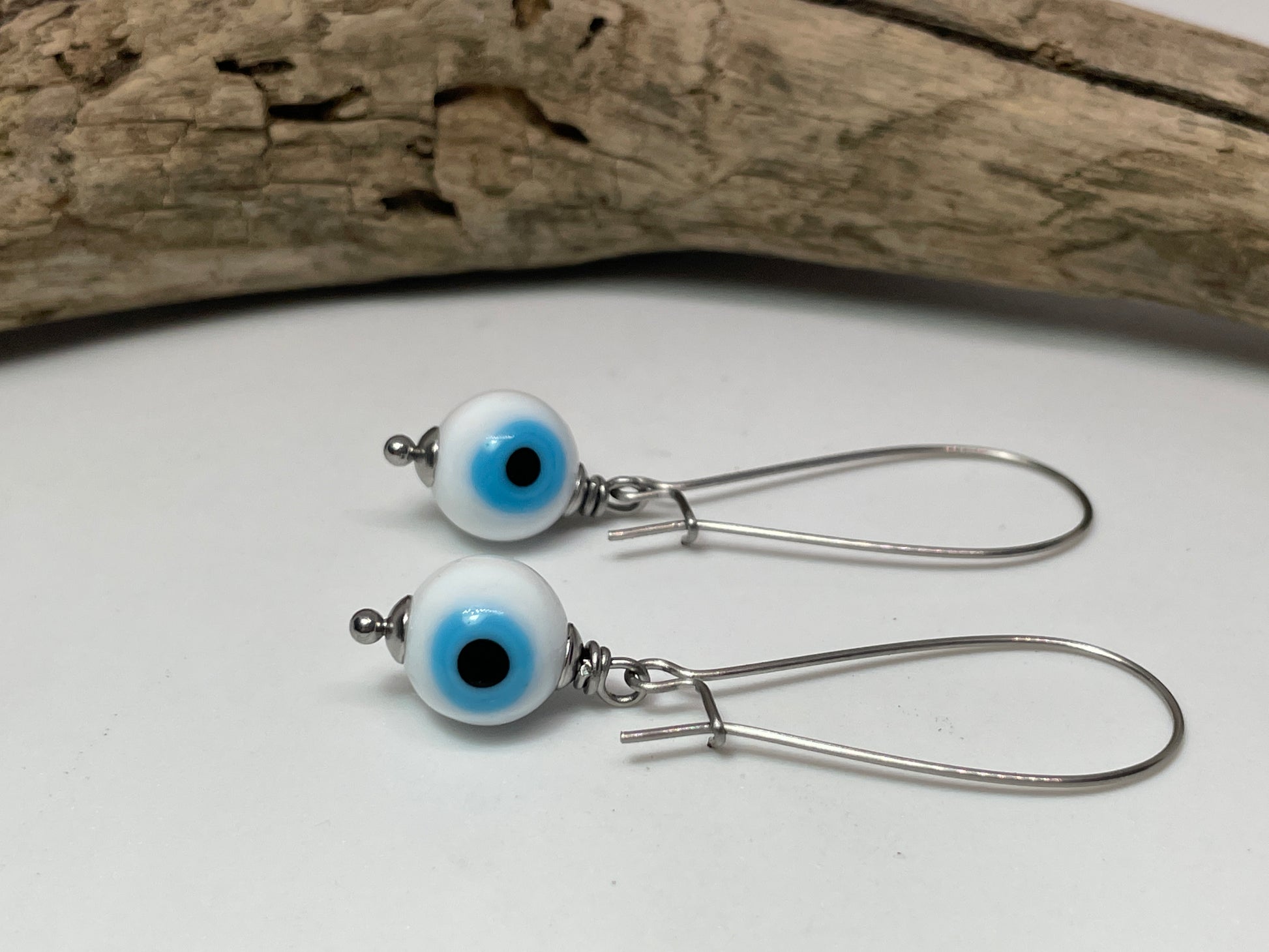 Pair of silver earrings with white beads featuring blue and black centers on a white surface.