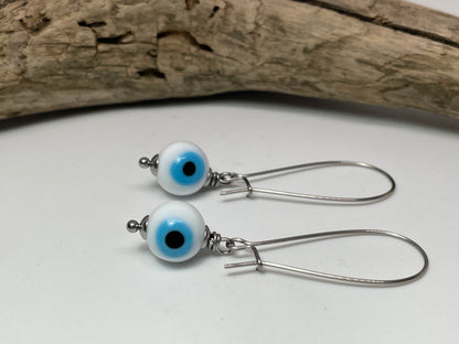 Pair of silver earrings with white beads featuring blue and black centers on a white surface.