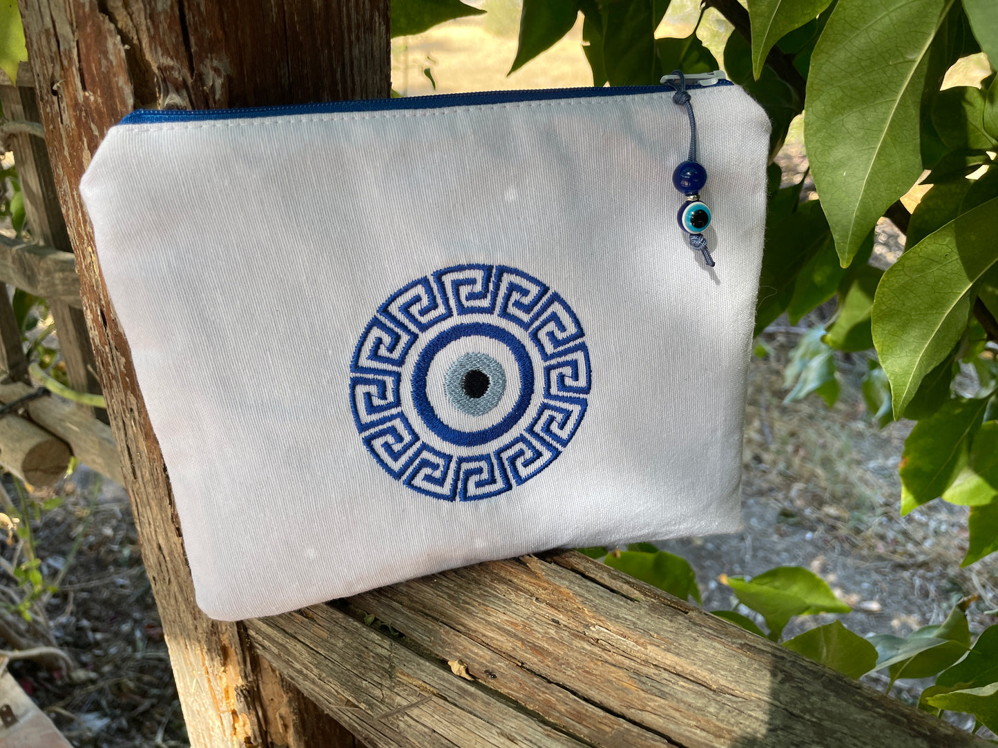 White pouch with blue decorative design hanging on a wooden post with greenery in the background