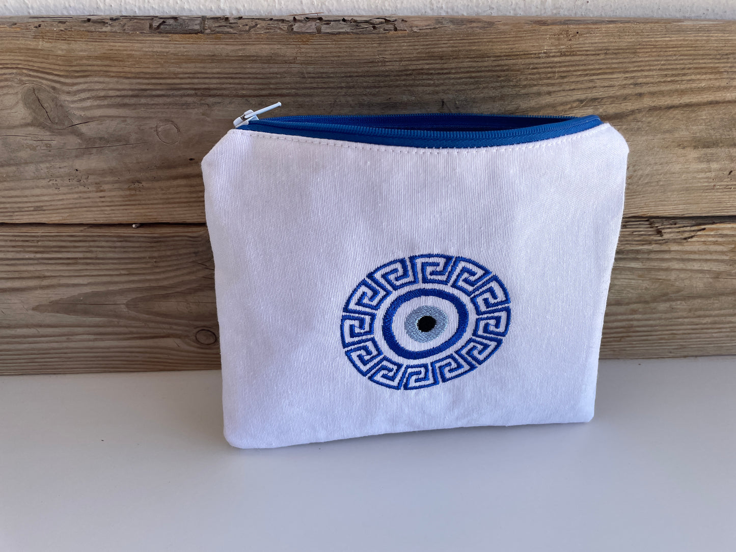 White pouch with blue zipper and Greek key design on a wooden surface