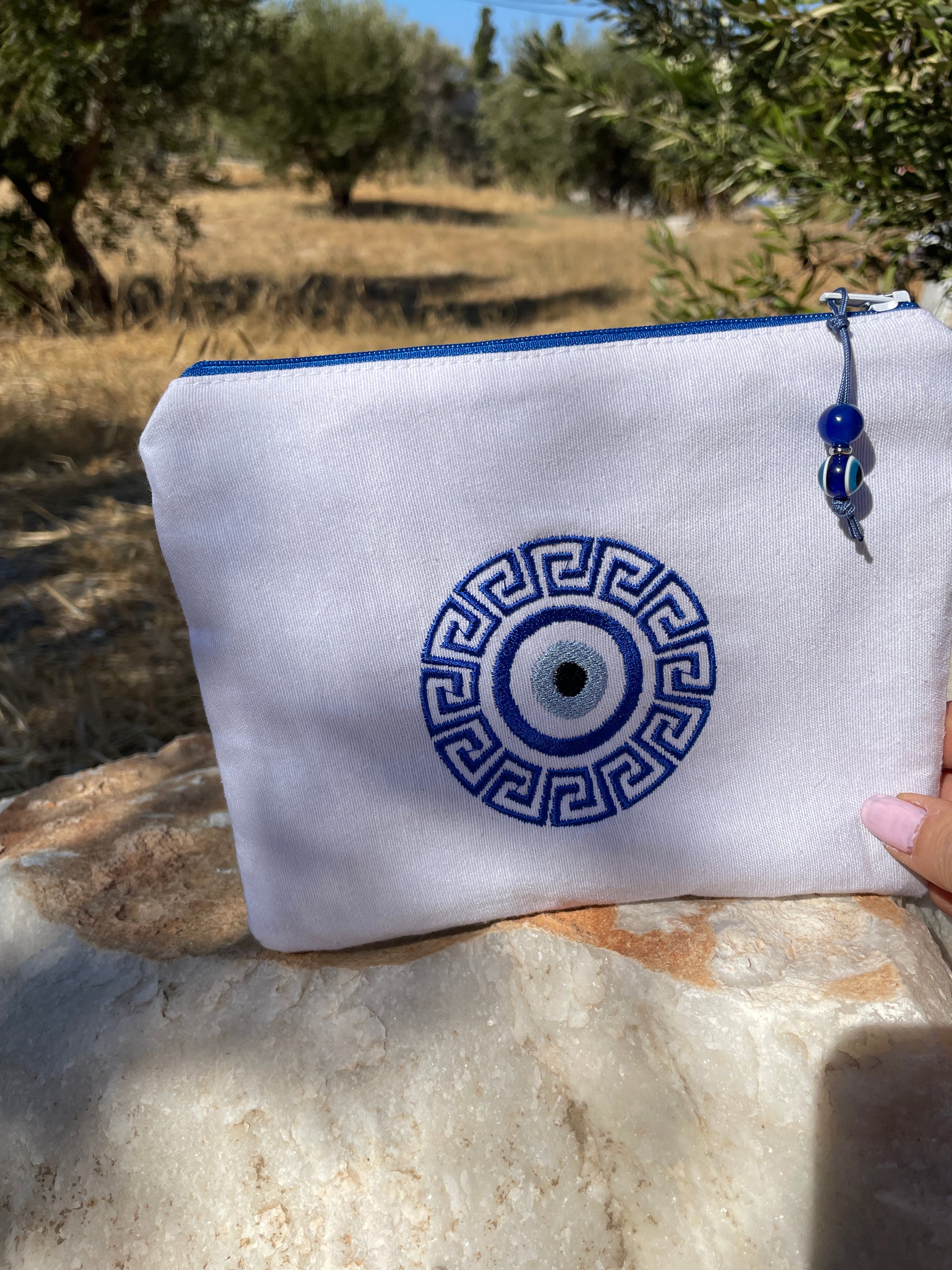White pouch with blue decorative pattern held outdoors on a stone surface