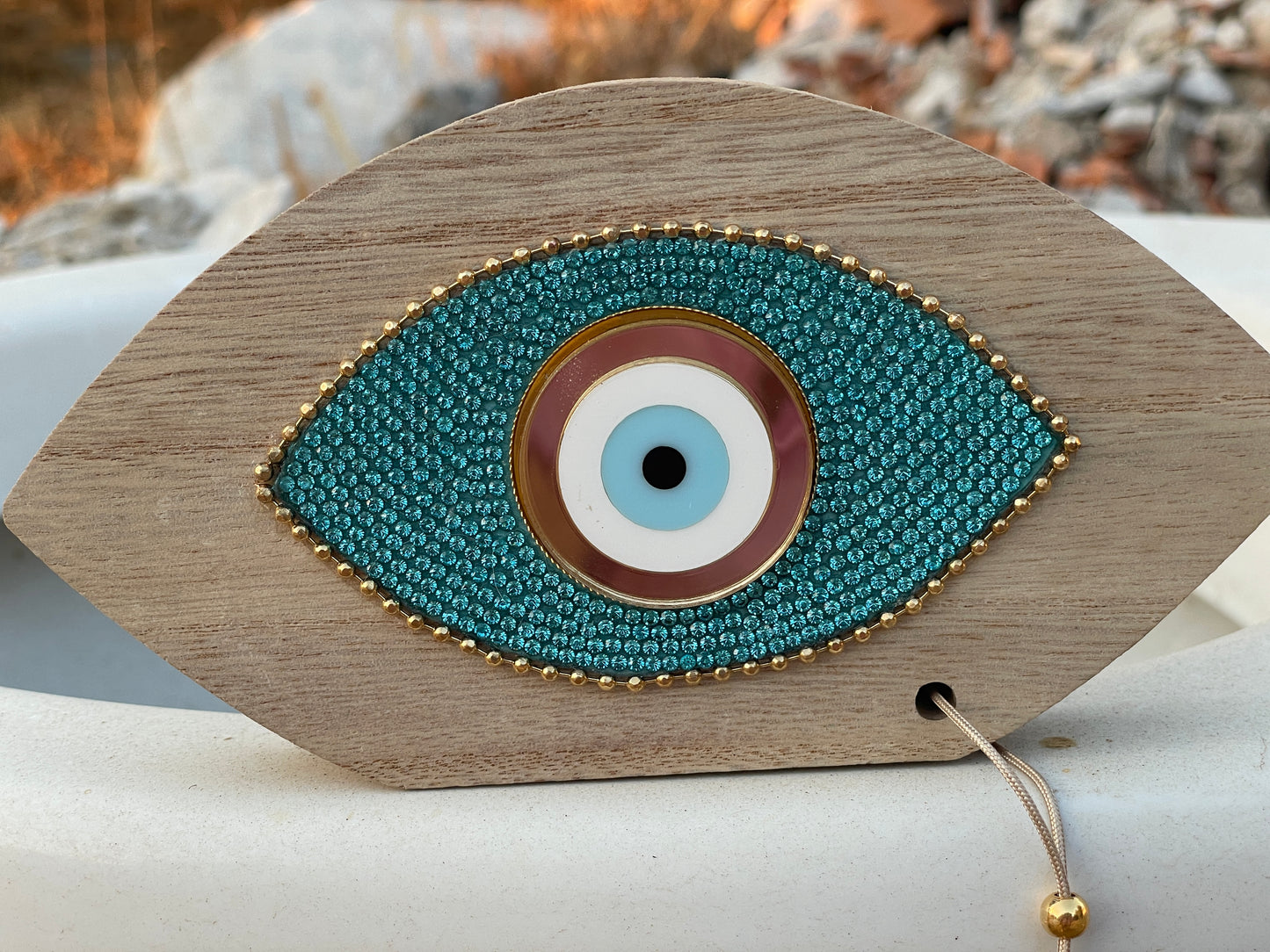 Decorative eye-shaped object with blue and gold details on a wooden base, set against a natural background.