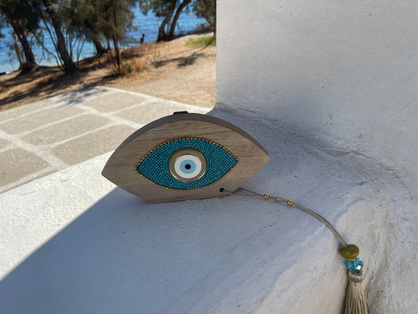 Decorative eye-shaped object with a tassel on a stone surface near a body of water.