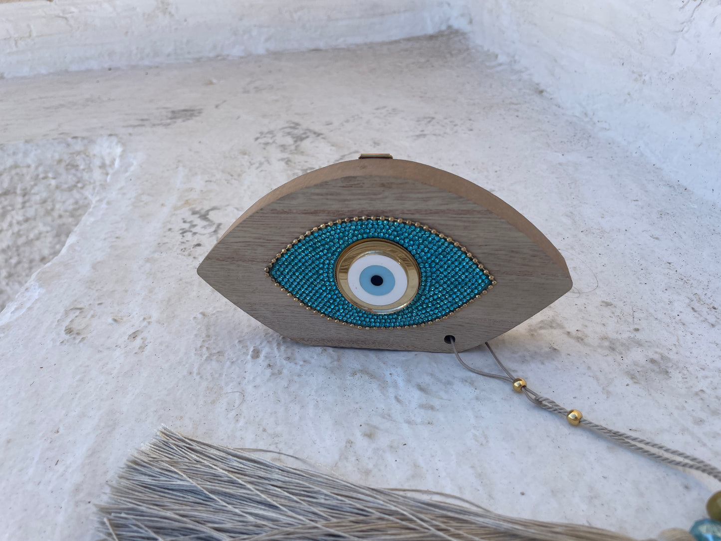 Wooden eye-shaped decorative item with blue bead detailing on a textured white surface