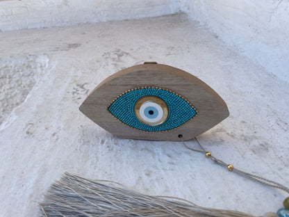 Wooden eye-shaped decorative item with blue bead detailing on a textured white surface
