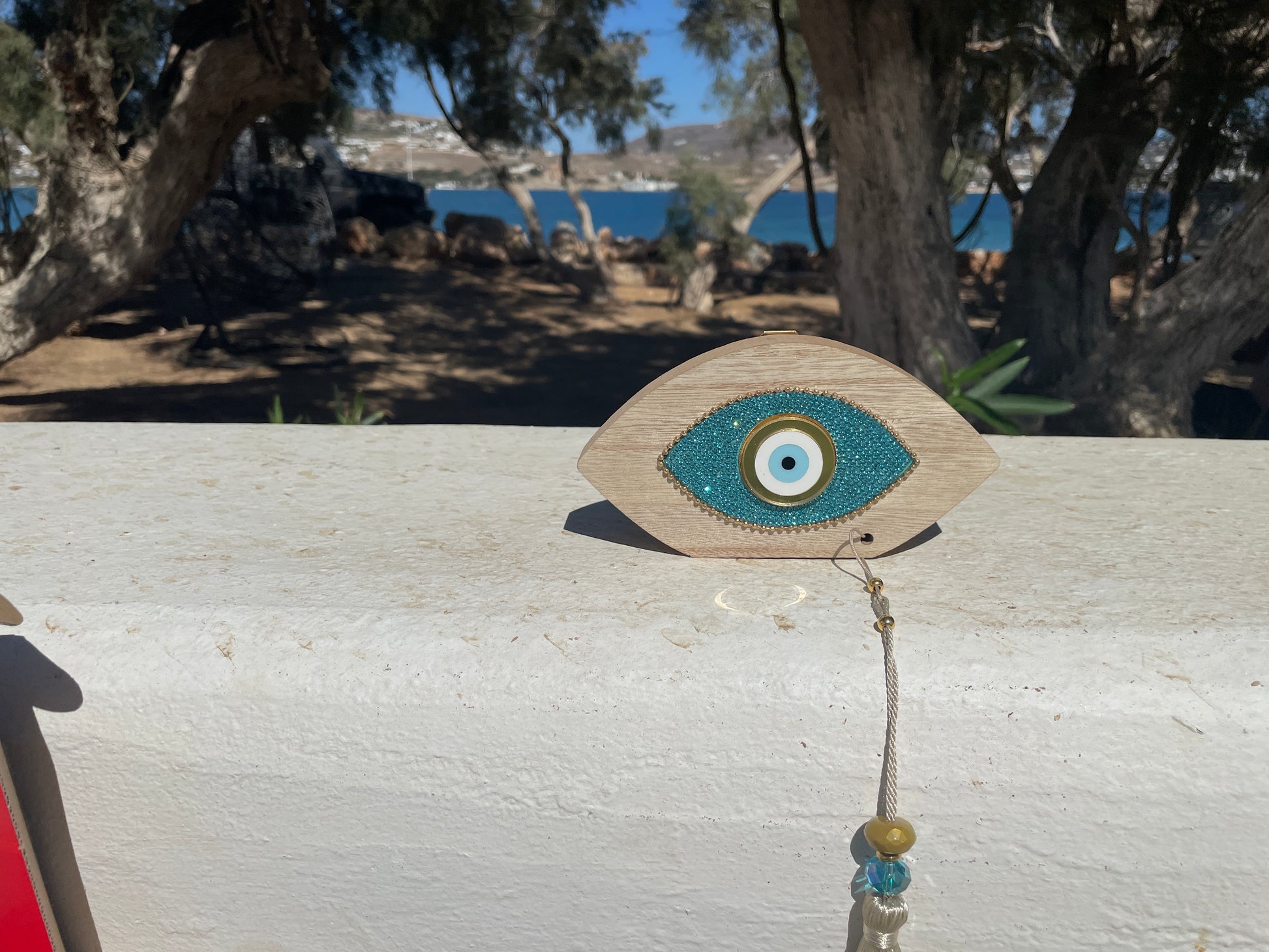 Decorative eye-shaped object with beads on a wooden surface near trees and water.
