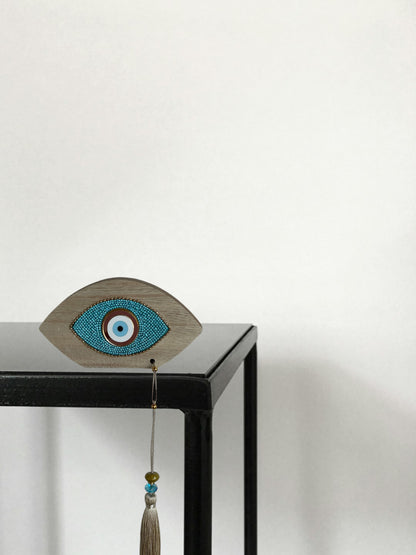 Decorative eye-shaped object with beads and a tassel on a black surface.