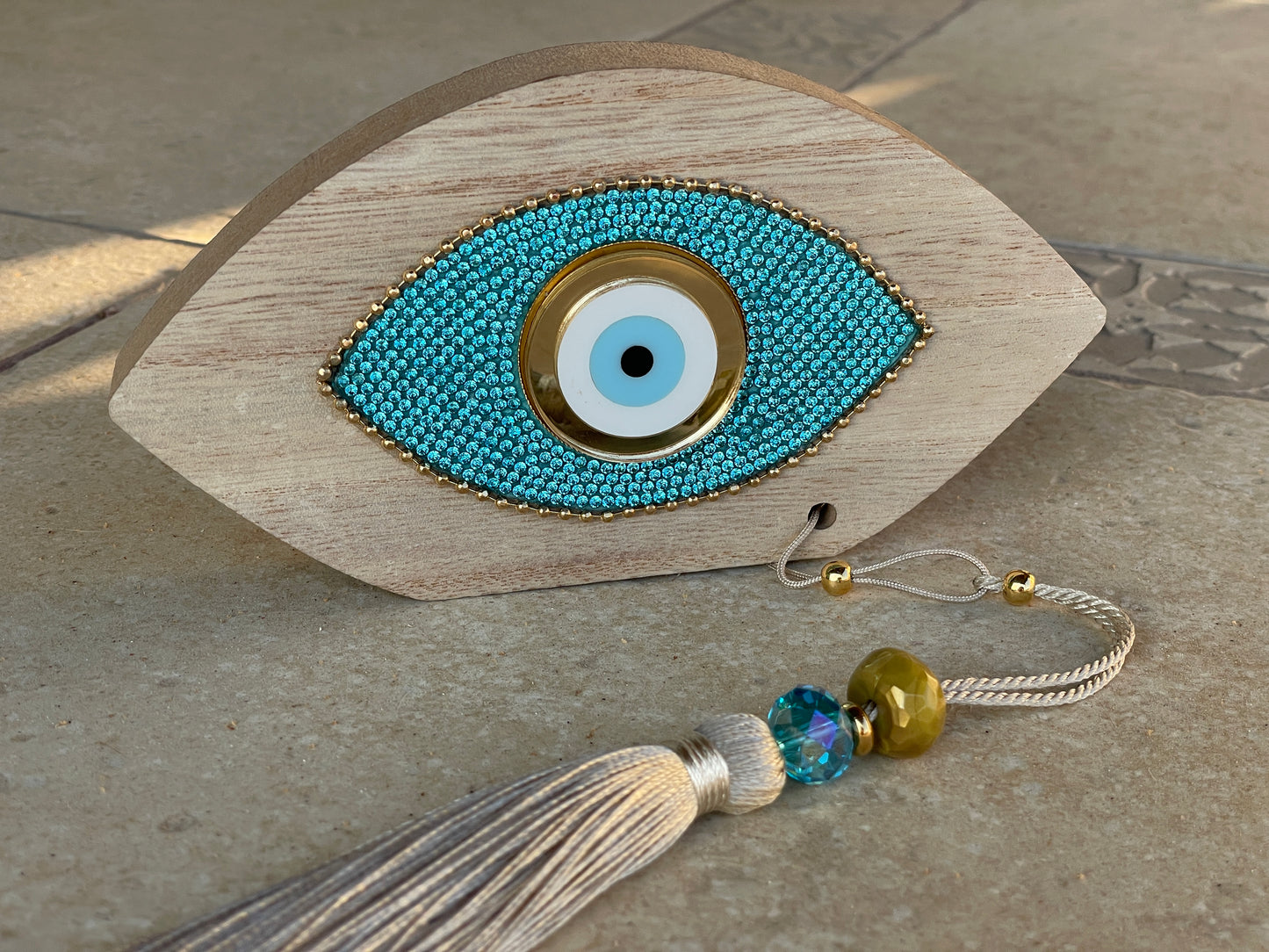 Decorative eye-shaped object with beads and tassel on a stone surface