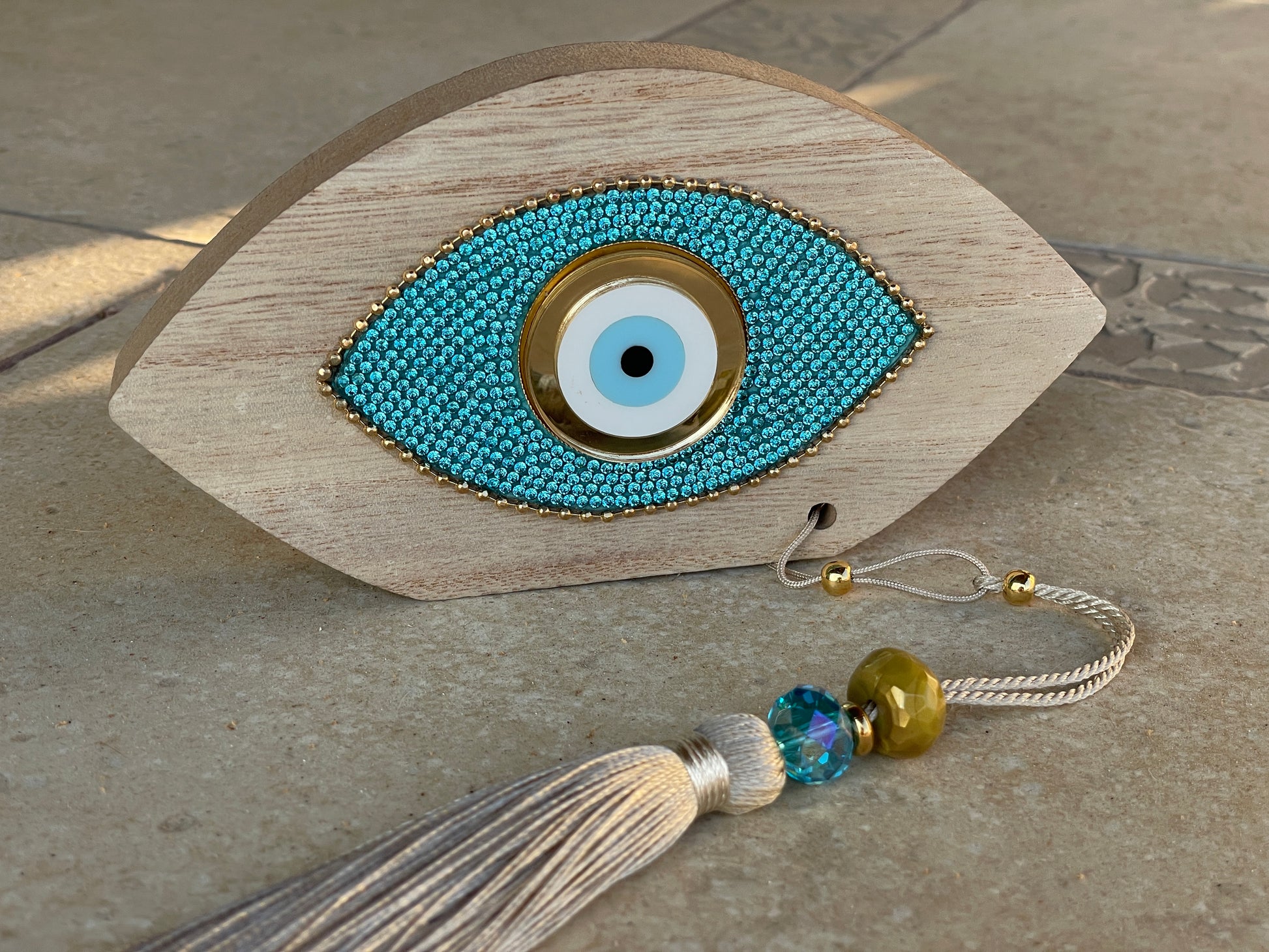 Decorative eye-shaped object with beads and tassel on a stone surface