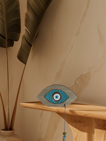 Decorative eye-shaped object on a wooden shelf with a plant in the background