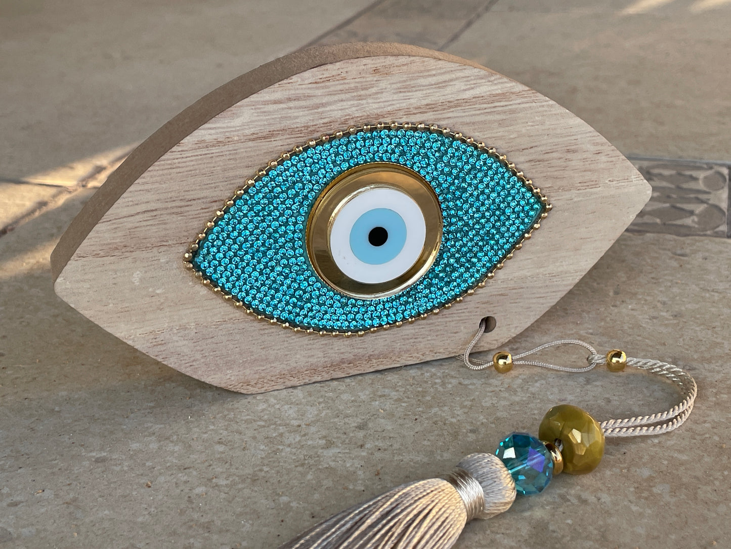 Decorative eye-shaped object with beaded design and tassel on a stone surface