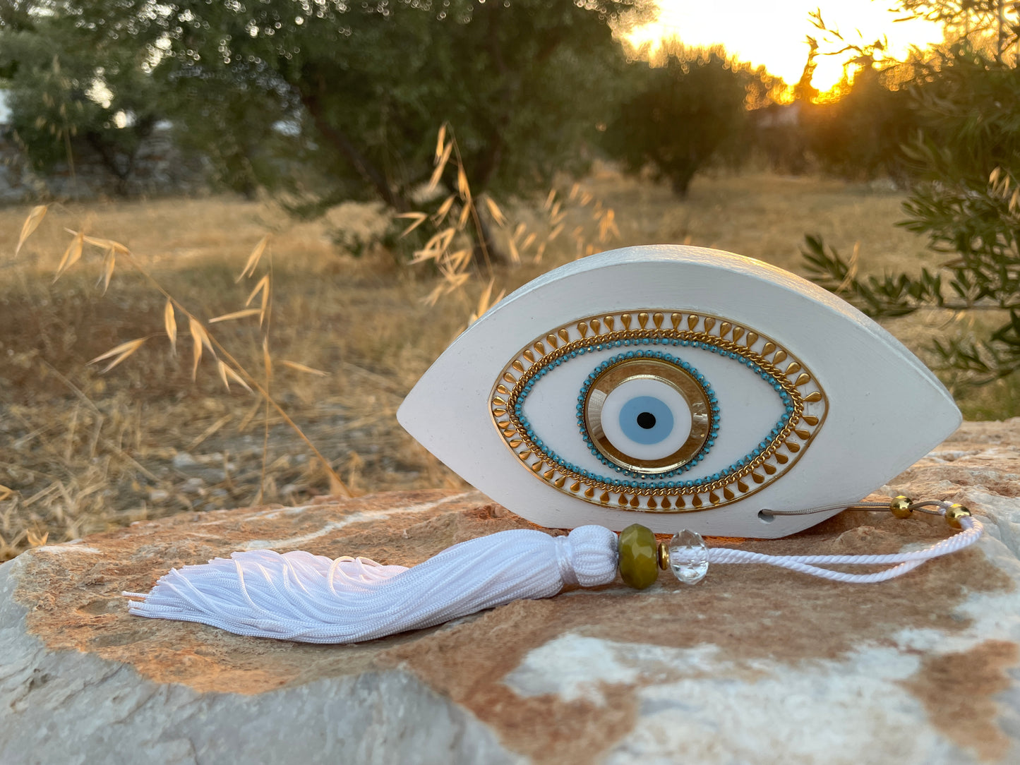Decorative eye-shaped ornament with tassel on a stone surface outdoors.