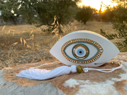 Decorative eye-shaped ornament with tassel on a stone surface outdoors.