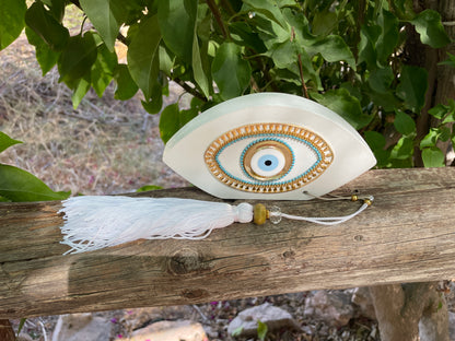 Decorative eye-shaped ornament with tassel on a wooden branch with green foliage in the background