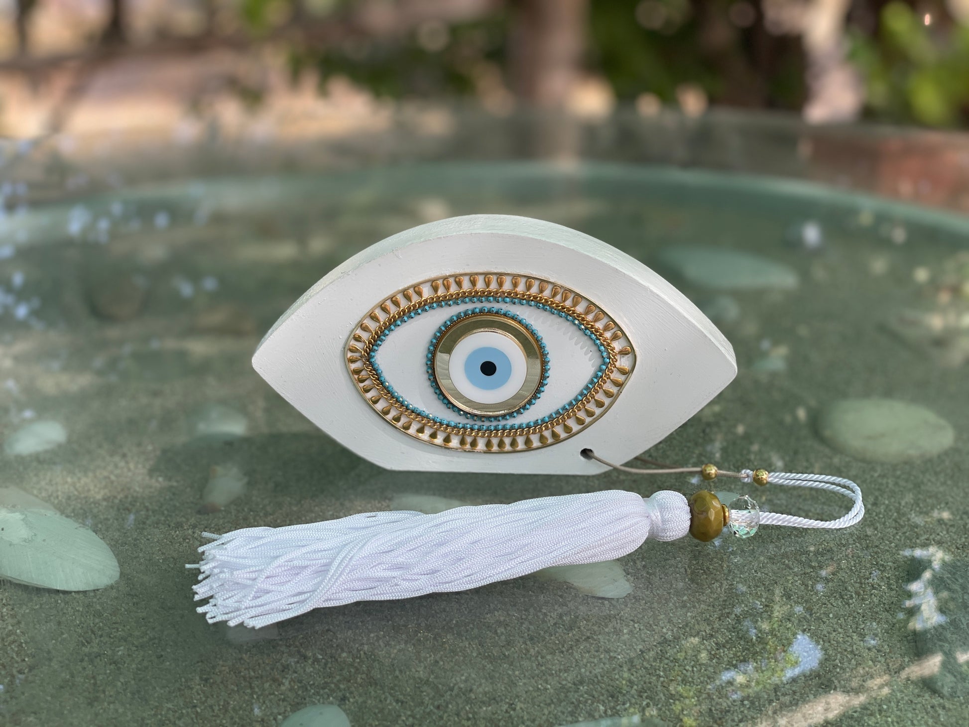 Decorative eye-shaped ornament with tassel on a reflective surface