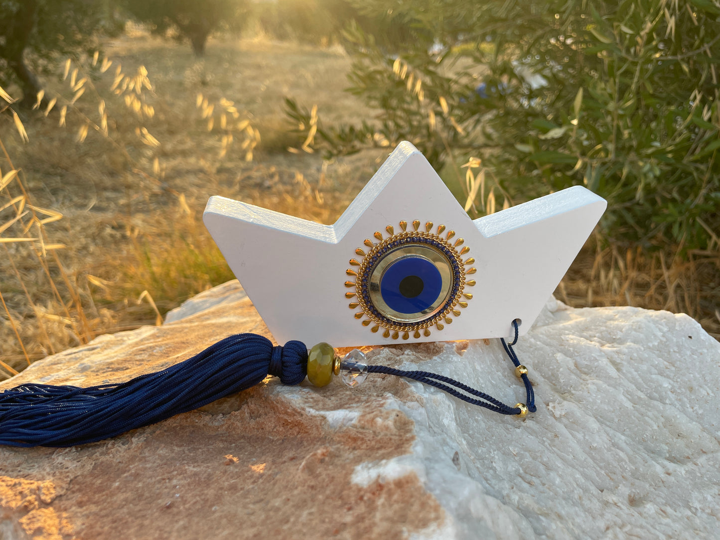 Decorative white star with blue eye design and tassel on a rock with natural background